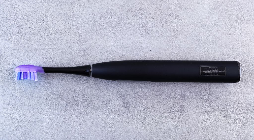 Black sonic electric toothbrush with a purple brush head on a concrete surface