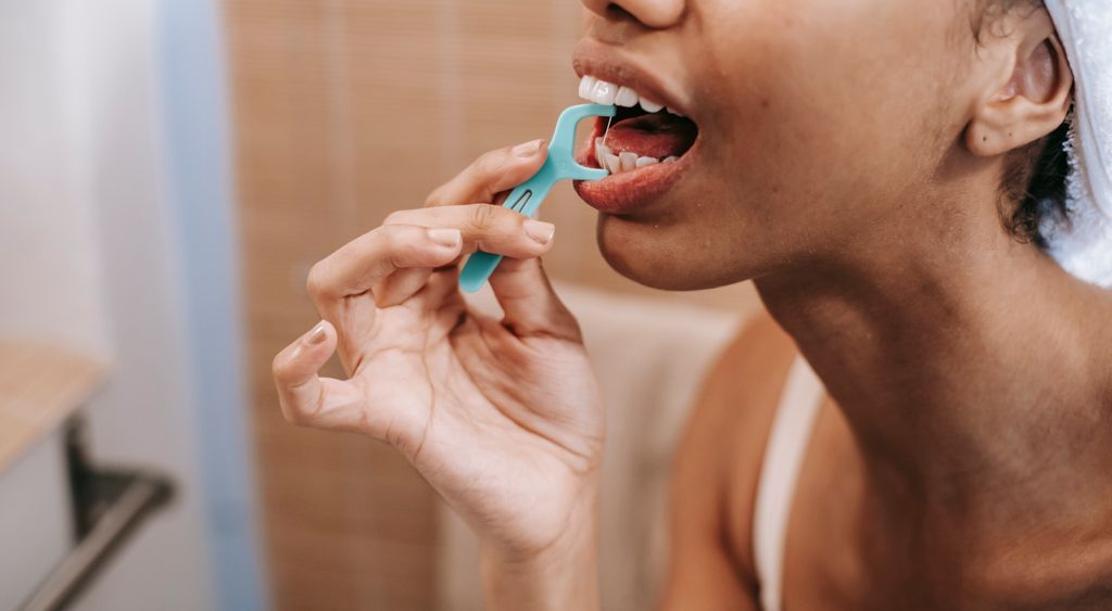 Person using a floss pick at the bathroom mirror